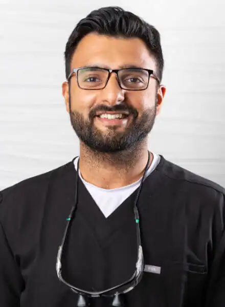 Dr. Jairahadeep Singh, Doctor of Dental Surgery at Zen Dental, smiling in dental scrubs with a dental loupes, promoting patient-centered care and comfort.