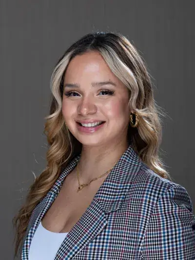 Illeana, Insurance Coordinator at Zen Dental, smiling in a professional setting, wearing a stylish checkered blazer and gold earrings.