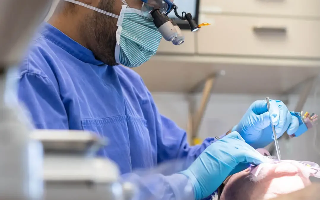 Dentist in blue scrubs and mask performing restorative dental procedure on patient in dental chair.
