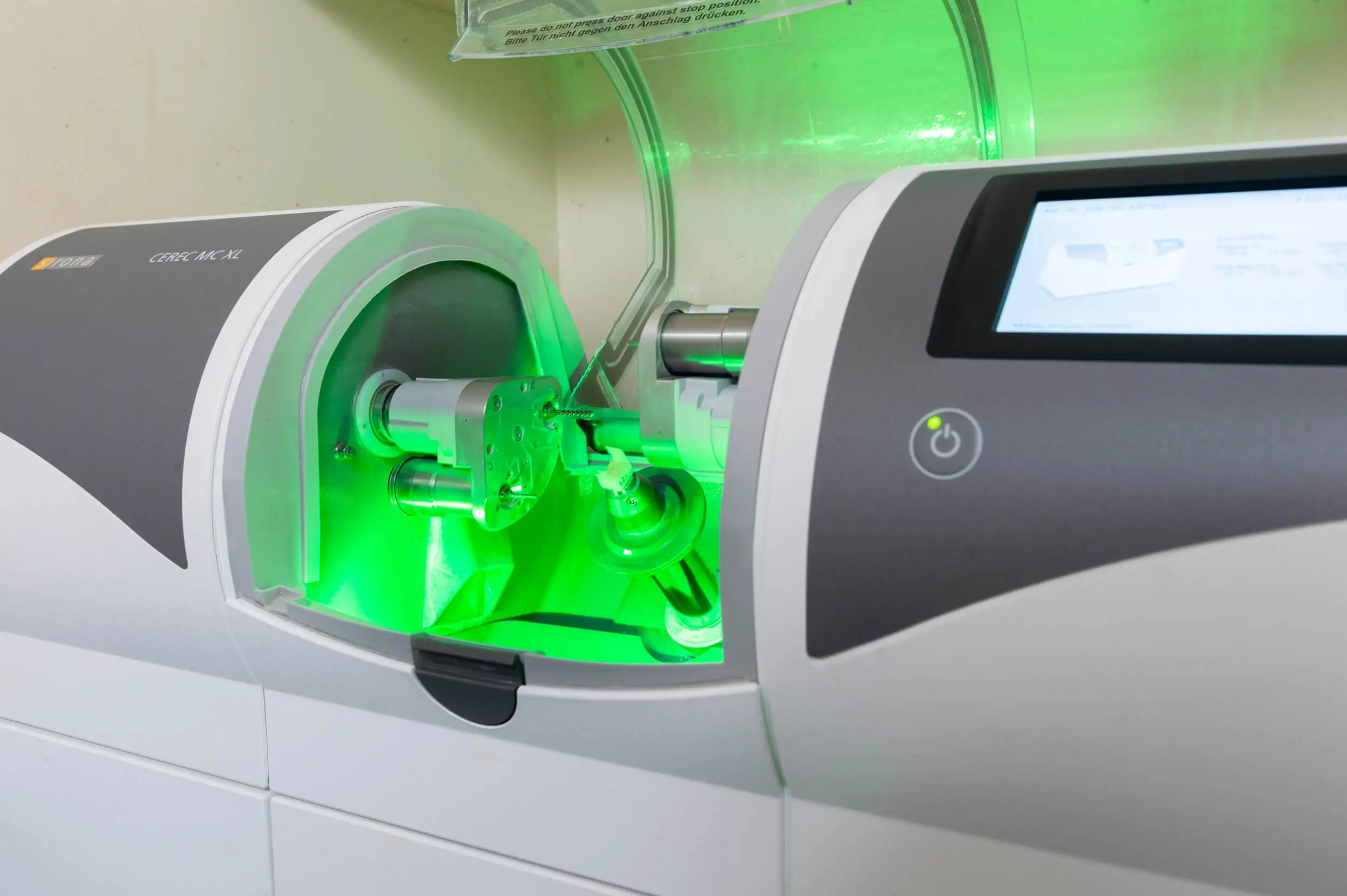 CEREC MC XL dental milling machine with green lighting, showcasing advanced technology for creating custom dental crowns at Zen Dental in Enfield, CT.